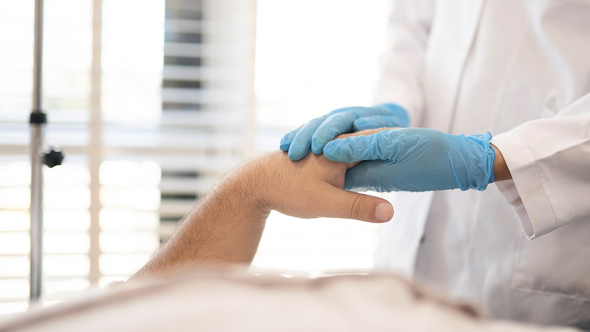 Doctor's hand with blue gloves are touching patient's hand.