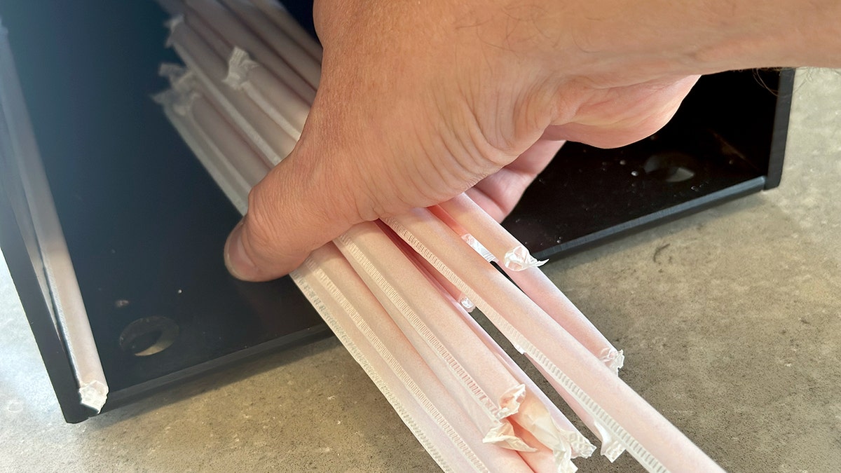 A hand grabs a clump of straws from a nearly empty container.