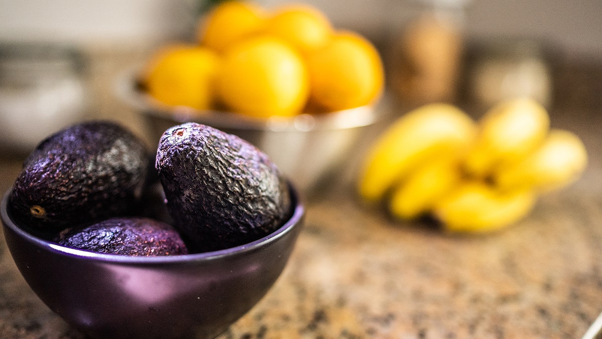 bowl with avocados in front of bananas and oranges