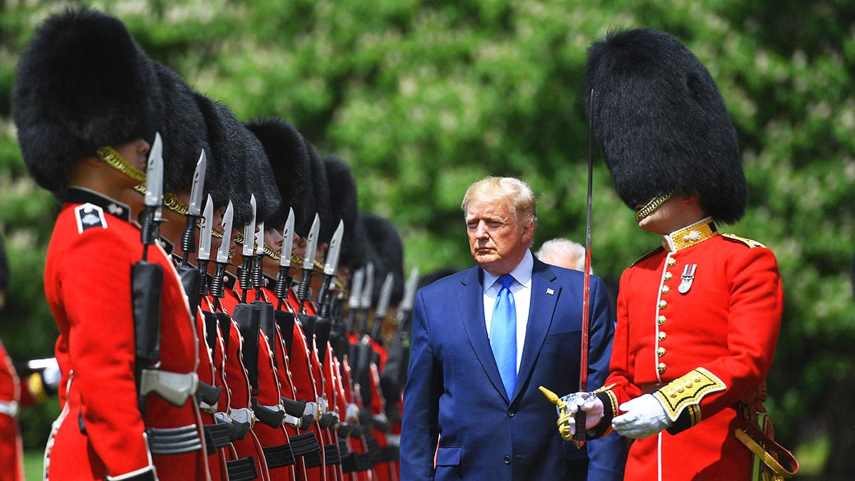 President Trump wearing a blue suit admiring the royal guards outdoors.
