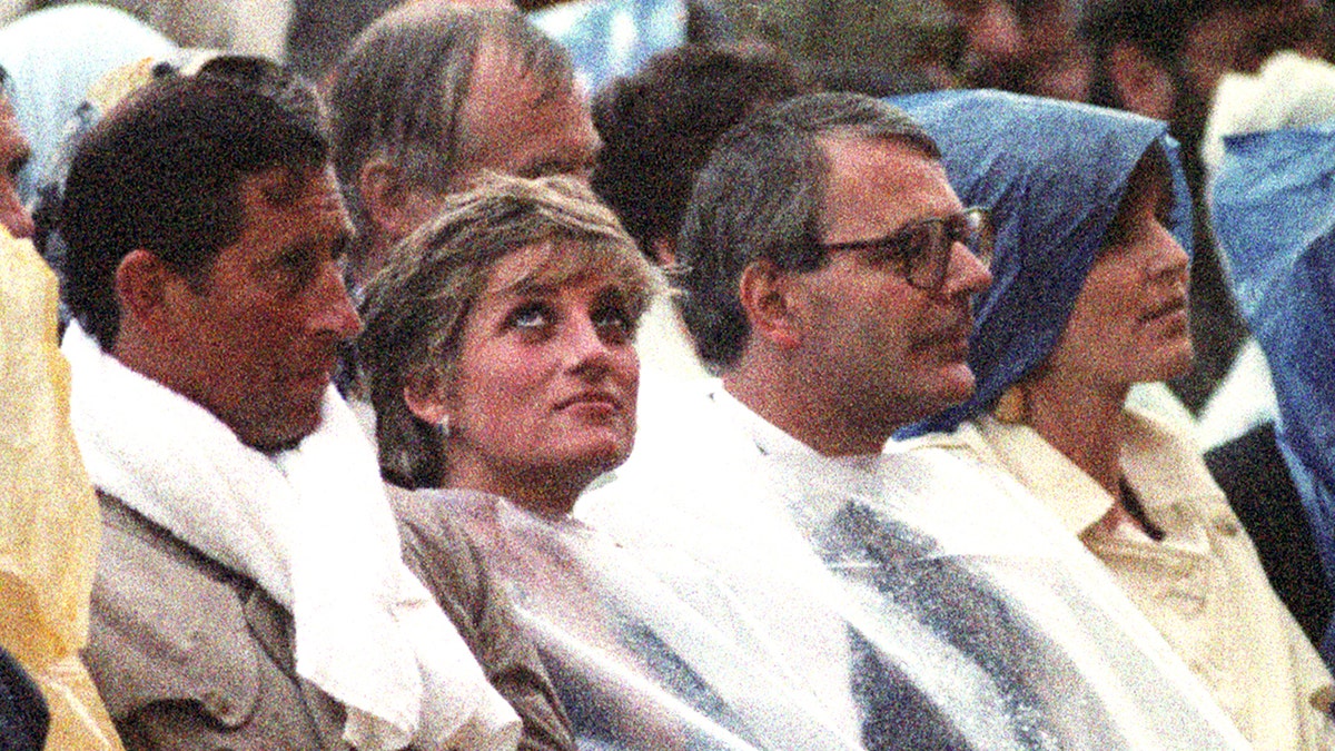 Prince Charles, Princess Diana and Sir John Major wet from the rain wearing clear ponchos.