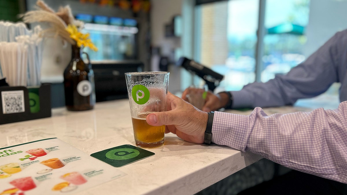 A hand holds a Publix glass with beer in it.