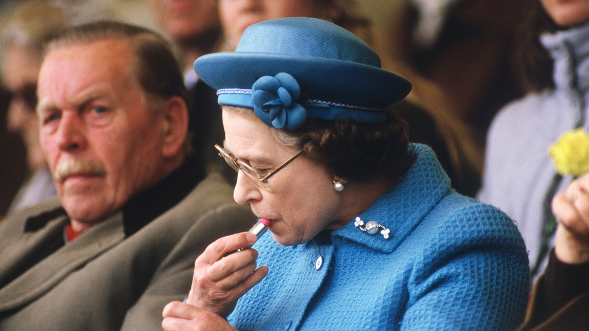 Queen Elizabeth applying lipstick.