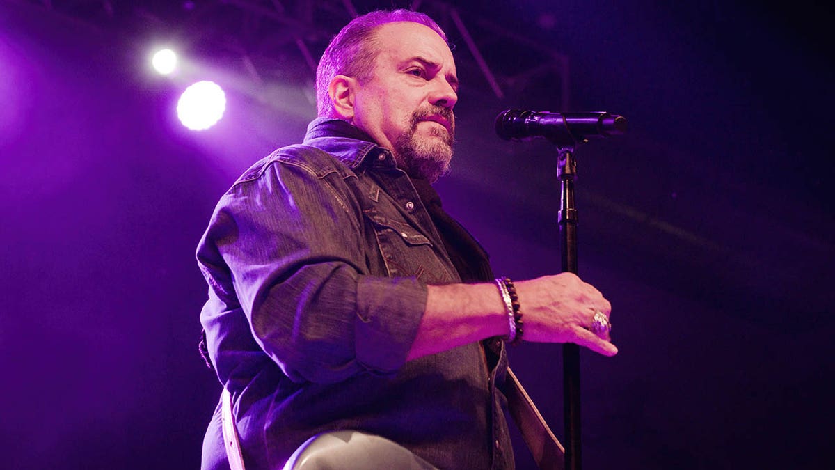 Raul Malo bir konser sırasında bir mikrofonun önünde duruyor. 