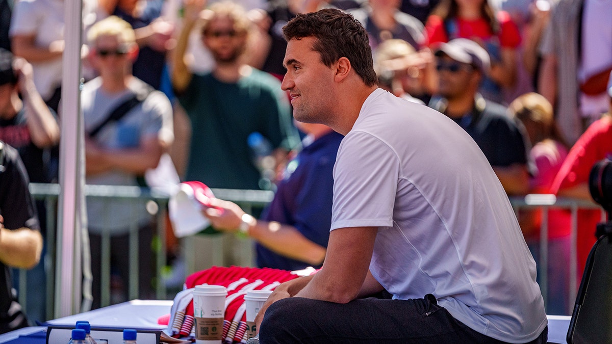 Charlie Kirk smiling next to Starbucks cup under tent