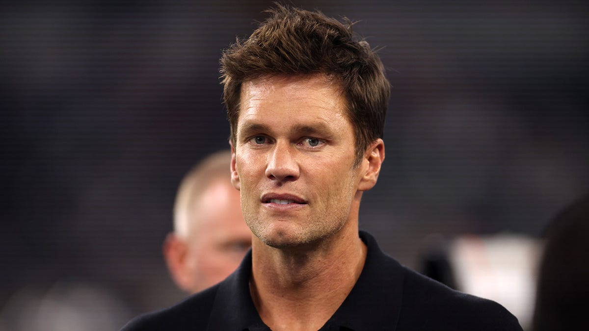 Tom Brady stands on a football field