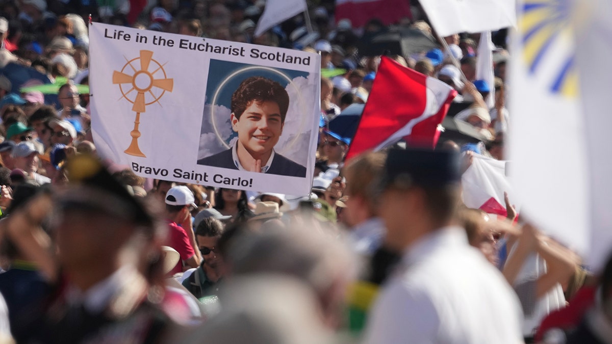 Crowd holding banners with pictures of Carlo Acutis