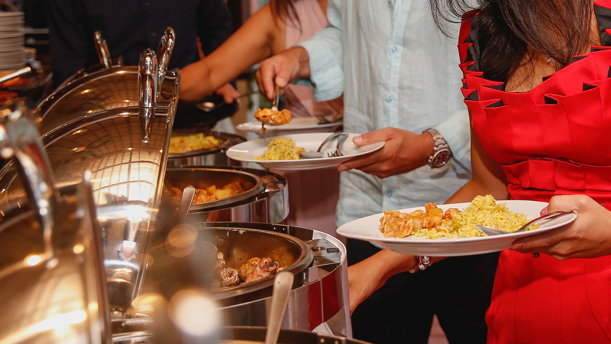 Wedding guests full plates with food at buffet, representing viral Reddit drama where woman brought her own food because of intolerances, was called "disrespectful" as a result.