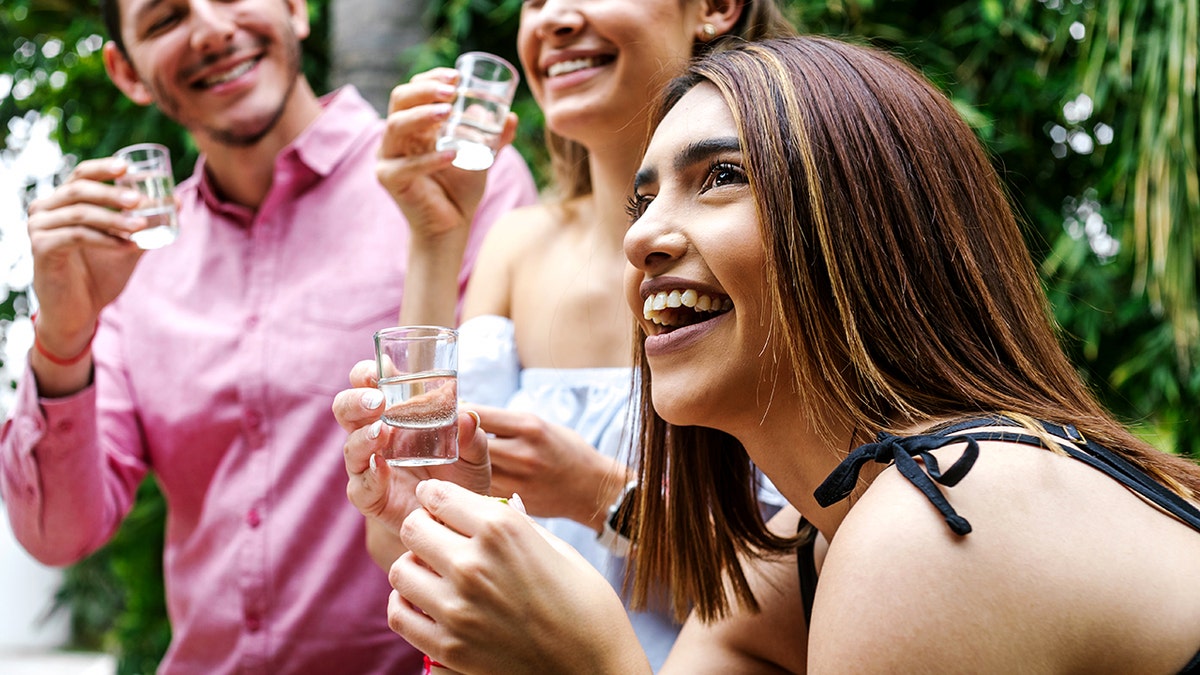 The woman holds tequila as two friends with tequila gun stops in the back.
