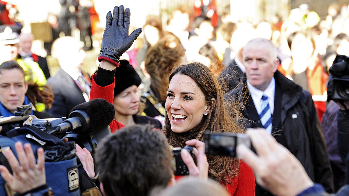 Kate Middleton smiling and waving to the public as photographers shoot pictures of her.
