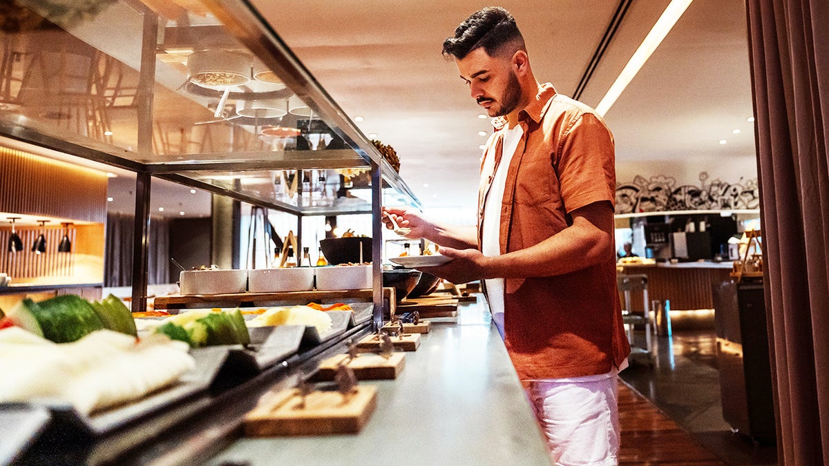 Man filling up plate of food at buffet counter in restaurant
