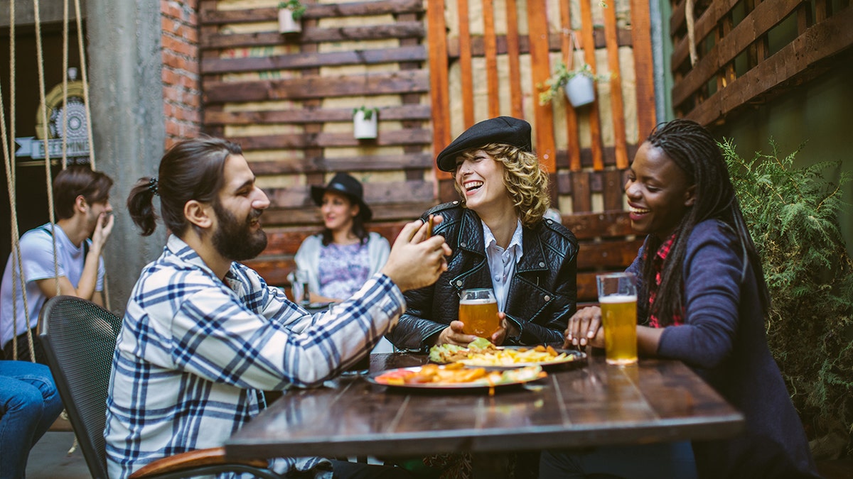 Three young people laughing at beer and food in bar/restaurant setting