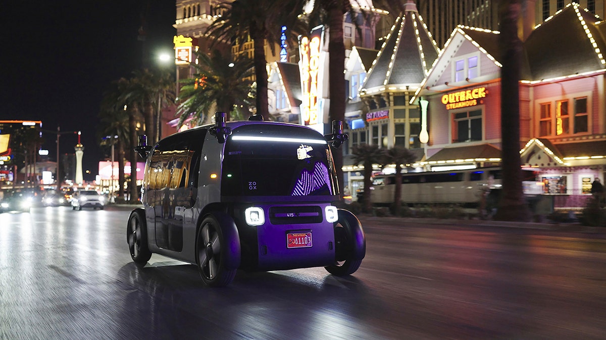 Amazon Zoox robotaxi seen driving down Las Vegas strip at night with cars, lights restaurants in background.