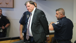 Rex Heuermann wearing a suit in court as two officers stand at his sides.