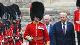 Donald Trump and King Charles walking together next to a royal guard.