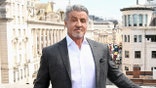 Sylvester Stallone standing on a balcony with a busy London street behind him.