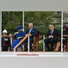 Queen Camilla smiles in a bright blue outfit as she sits next to King Charles III and Donald Trump during a royal ceremony.