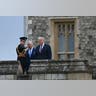 King Charles and Donald Trump listen to a British officer in full dress uniform pointing across the castle grounds.