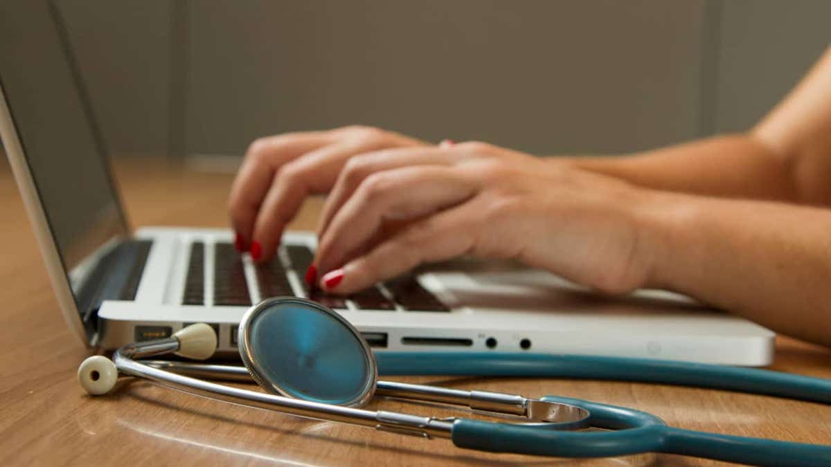 SimonMed data breach affects 1.2M patients in nationwide cyberattack 1 Hands typing on a laptop keyboard with a stethoscope resting on the desk