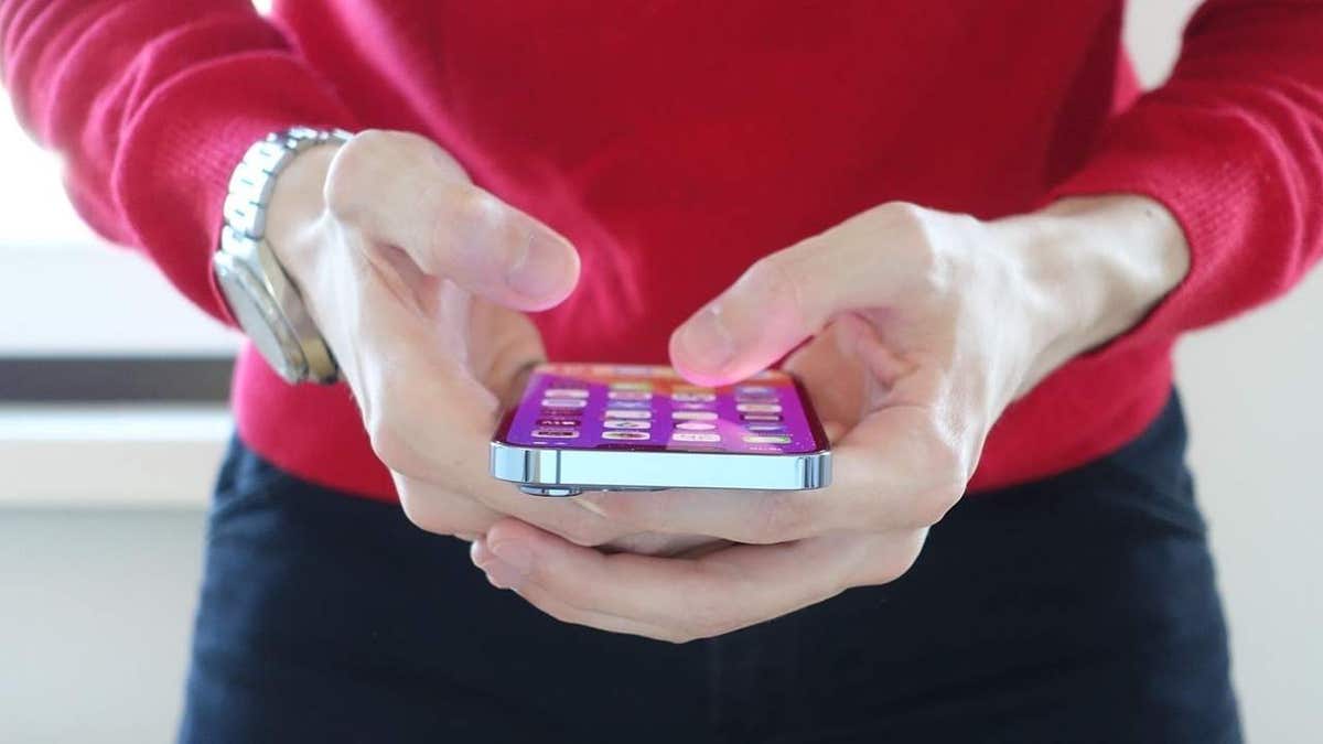 Wi-Fi calling may drain iPhone battery faster than cellular connection 1 A person in a red sweater holds a smartphone with a colorful home screen, typing on the device.