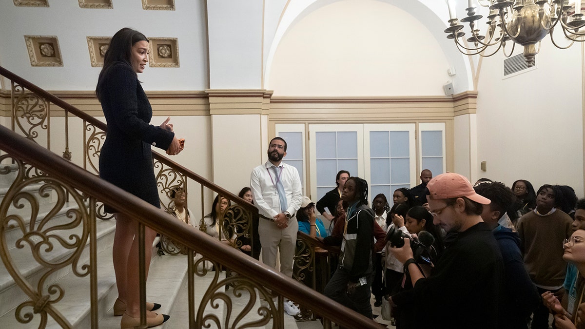 Alexandria Ocasio-Cortez standing on staircase speaking with students on tour of Capitol