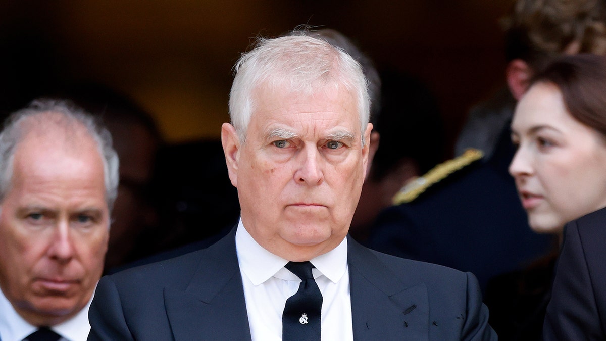A close-up of Prince Andrew looking serious in between two people outside of church.