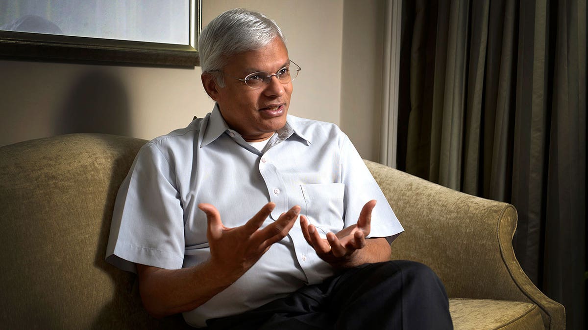 Man with gray hair and glasses gestures while speaking in Mumbai, India.