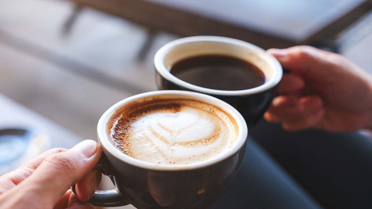 Closeup image of a man and a woman clinking coffee mugs in cafe