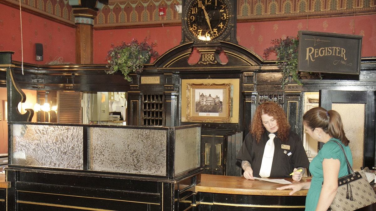 A woman checking in at the front desk at Crescent Hotel and Spa with a female employee, old decor, clocks in background.