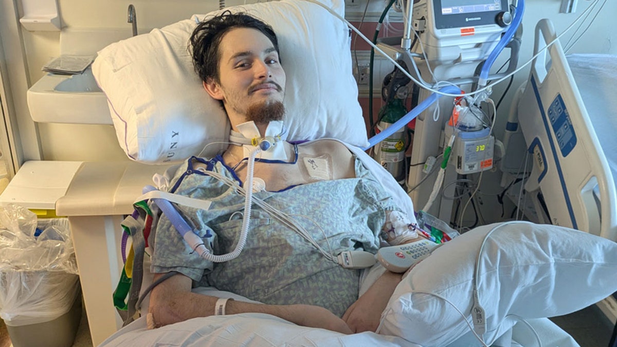 Daniel Waterman smiling in hospital bed as he's hooked up to various machines