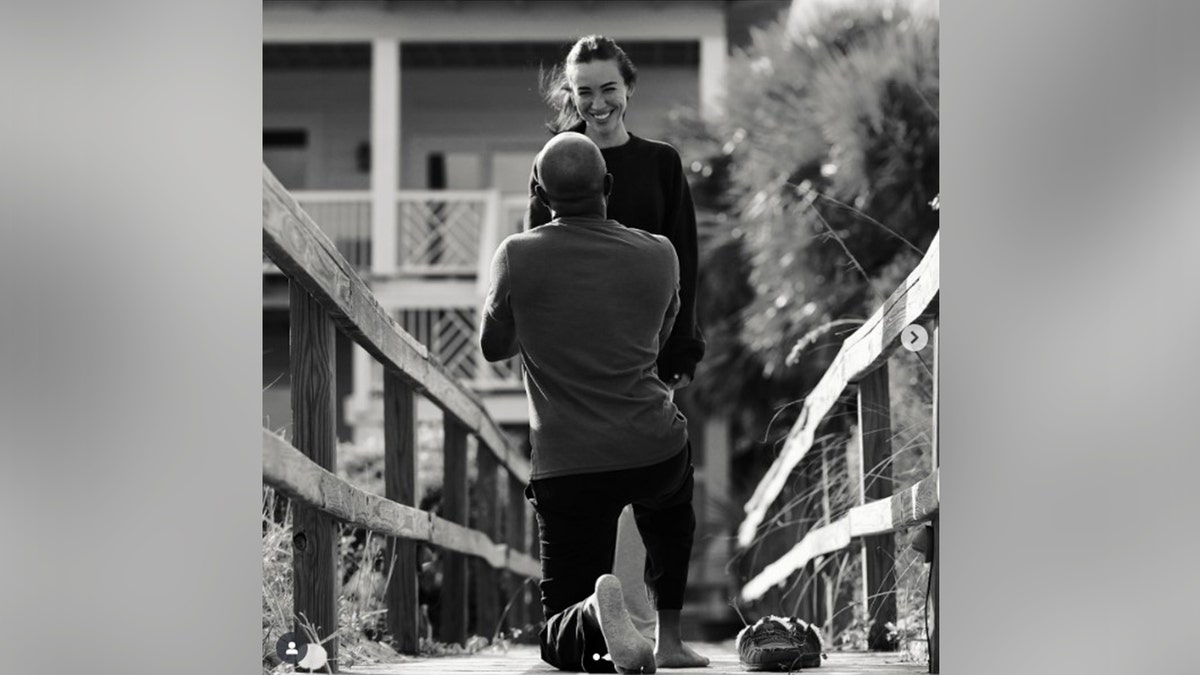 A black and white photo of Darius Rucker from behind as he proposes to his girlfriend.