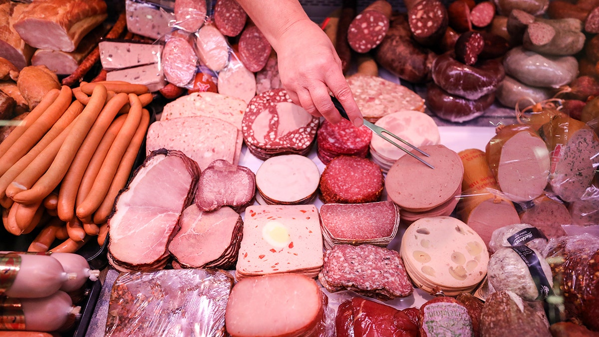 Hand of a saleswoman taking sliced meats from a counter in a supermarket.