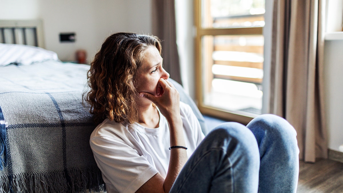 Young adult woman with depression sitting at home alone