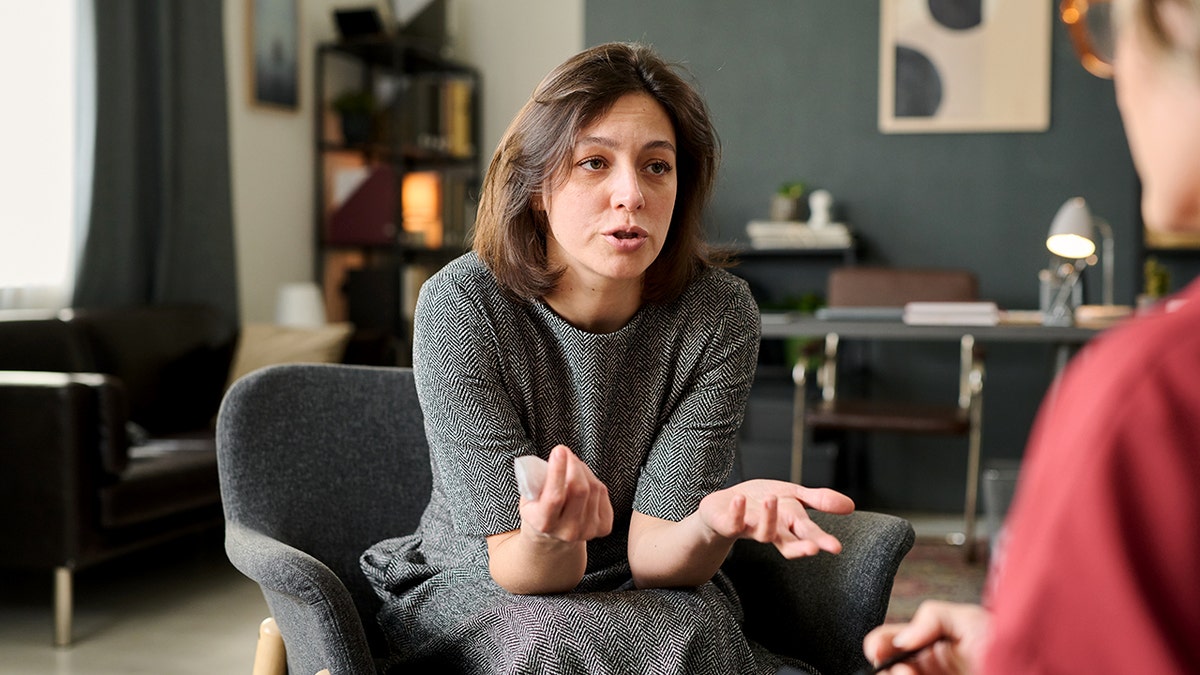 Woman sitting in comfortable chair engaging in conversation with other person in office setting