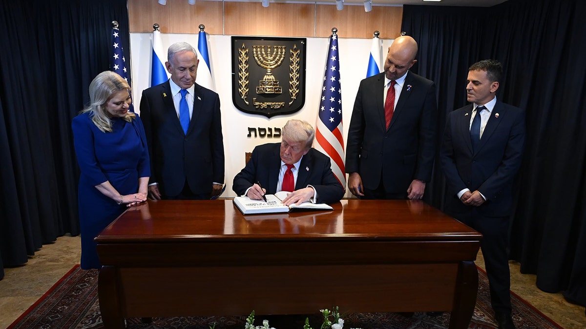 Donald Trump siedzi przy biurku w Knesecie i wpisuje się do księgi gości z premierem Izraela Benjaminem Netanjahu i innymi oglądającymi