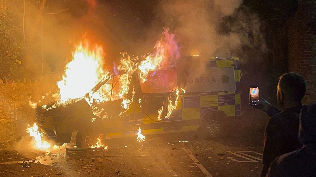 Burning Garda vehicle during violent Dublin protest outside asylum seeker hotel.