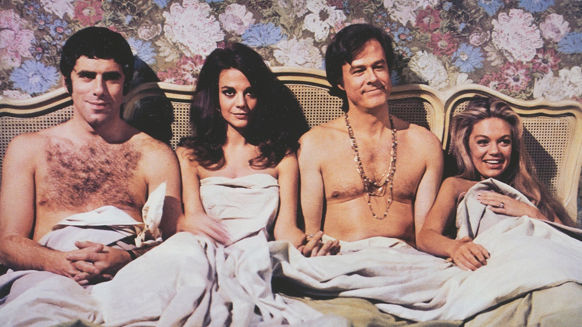 Dyan Cannon in bed with her co-stars acting out a scene from a 1969 film.