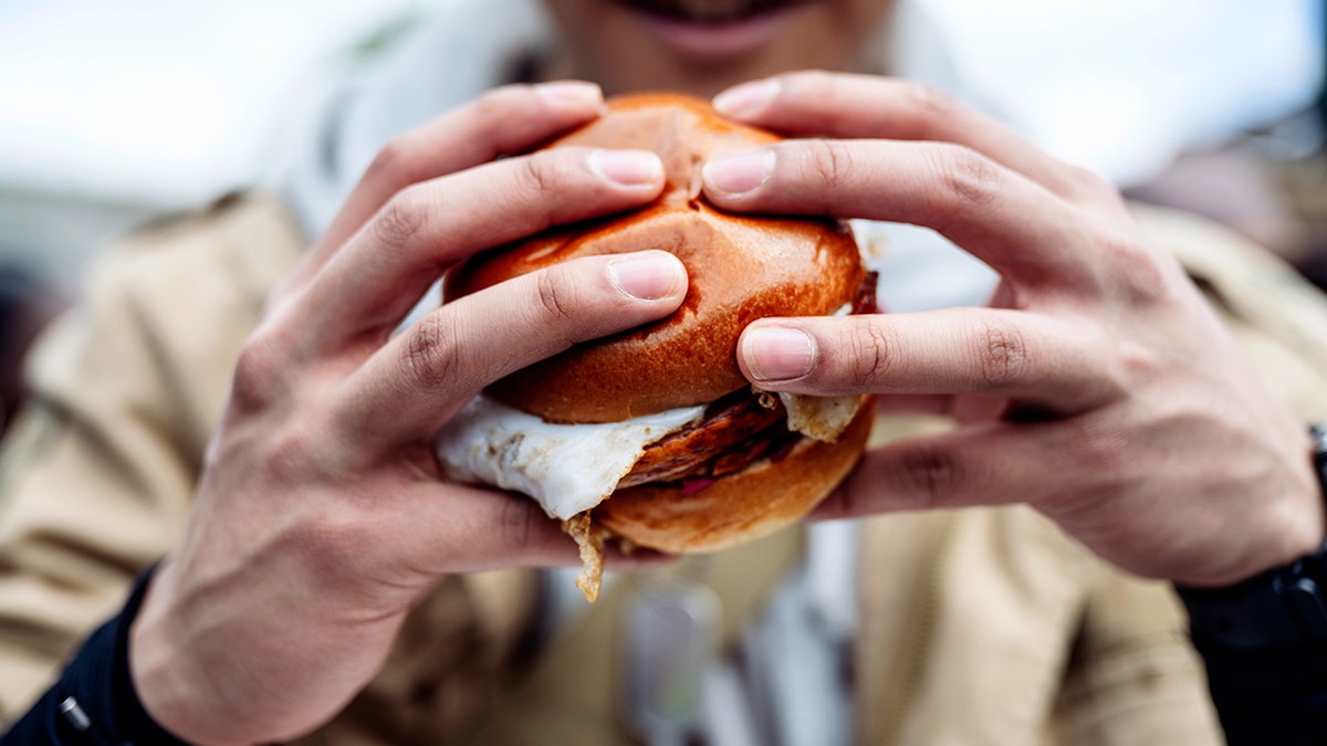 A man's hands hold an egg sandwich.