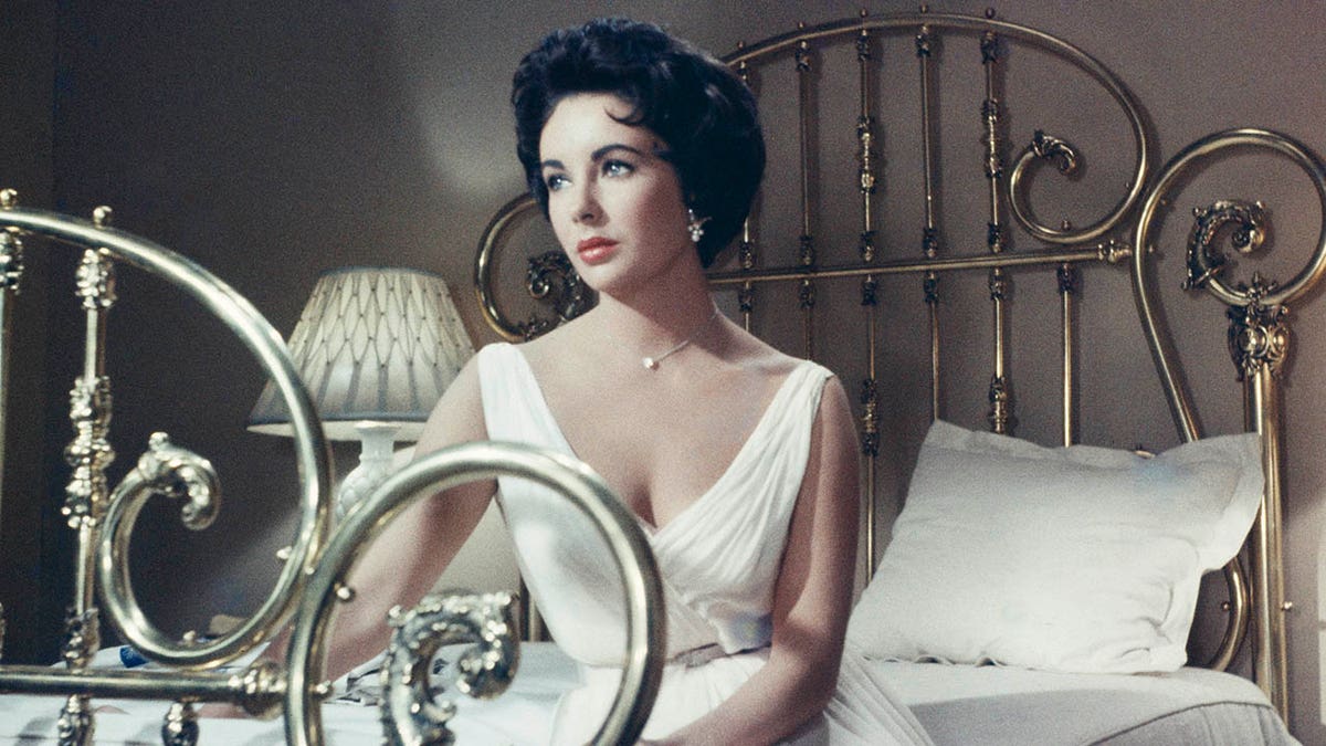 A 1958 photo of Elizabeth Taylor sitting on a bed. 