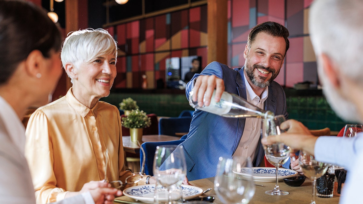 Four business people smiling at restaurant, as one man pours another glass bottle of water.