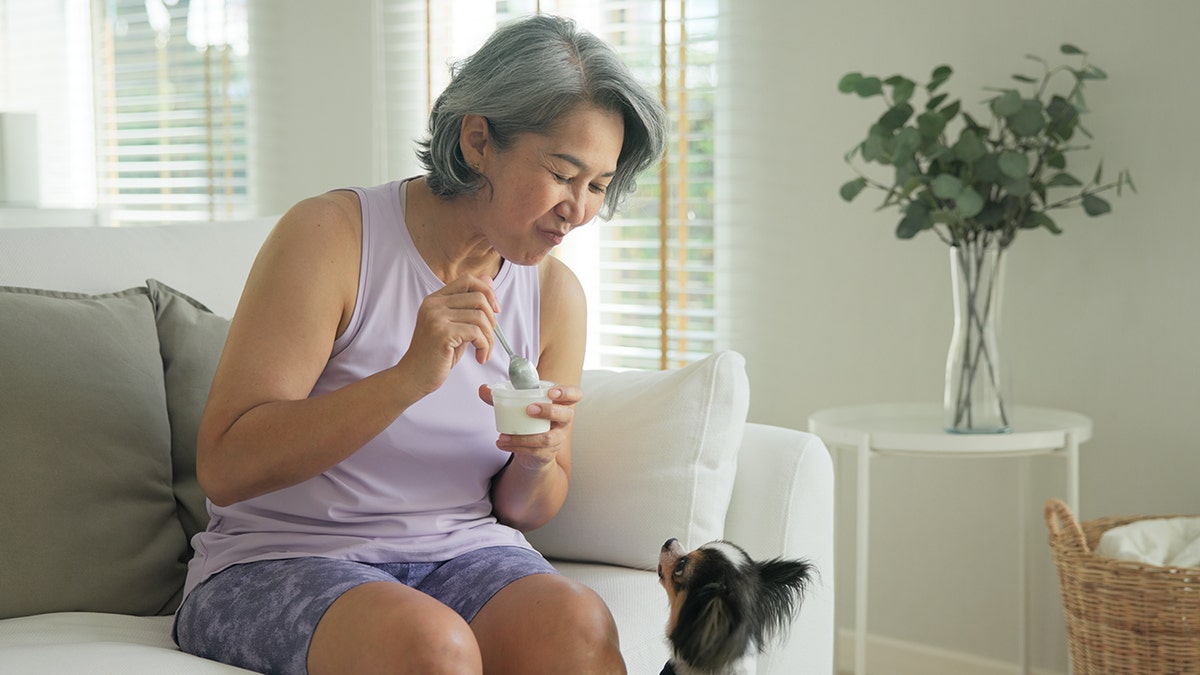 Older woman eating yogurt next to dog