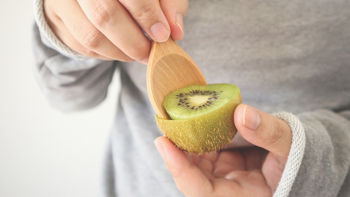 Person eating kiwi fruit with spoon