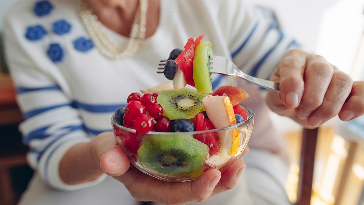 Older woman eating fruit salad with kiwis
