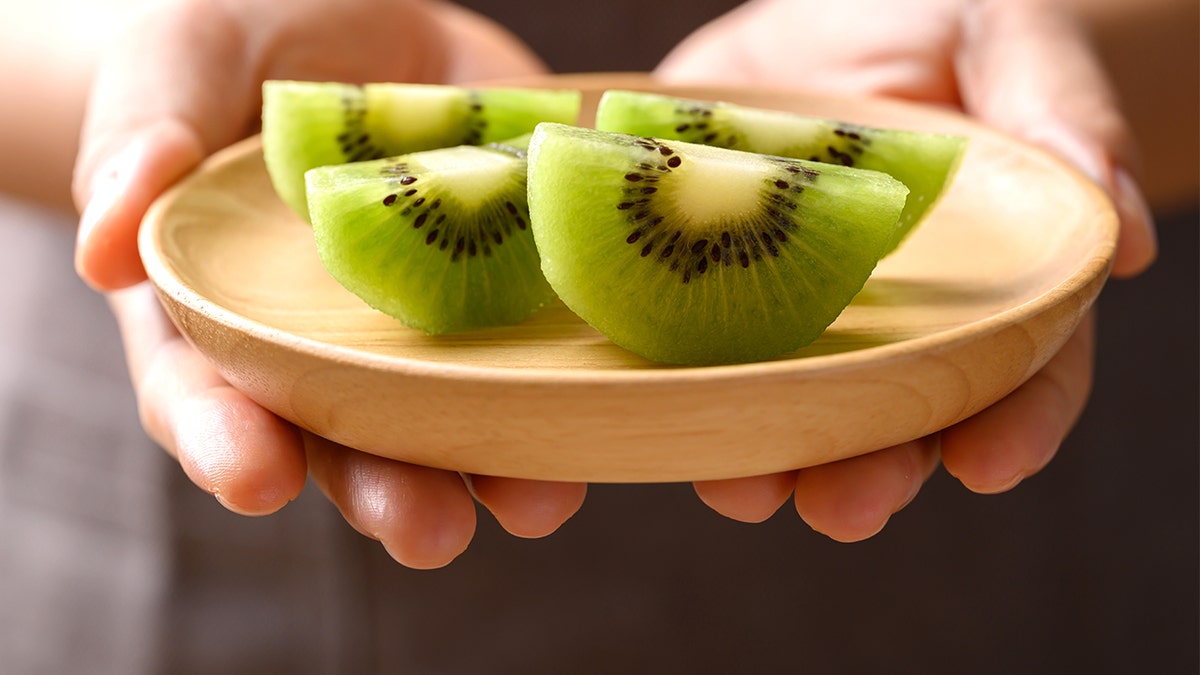 Person holding a plate of sliced kiwis