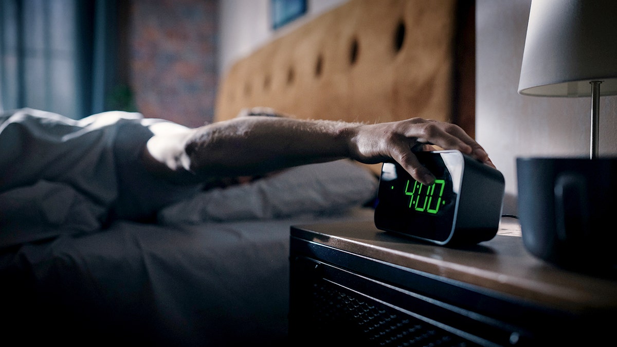 man turns off alarm clock reading 4:00