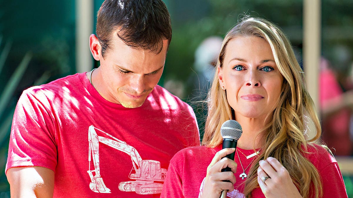 Granger Smith looking down crying as Amber Smith holds a mic while fighting back tears.