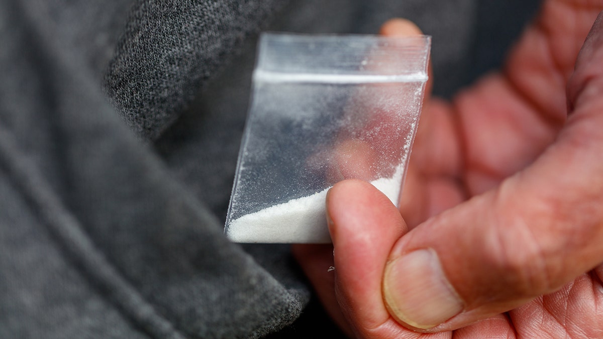 A hand holding white powdery drugs in a small bag