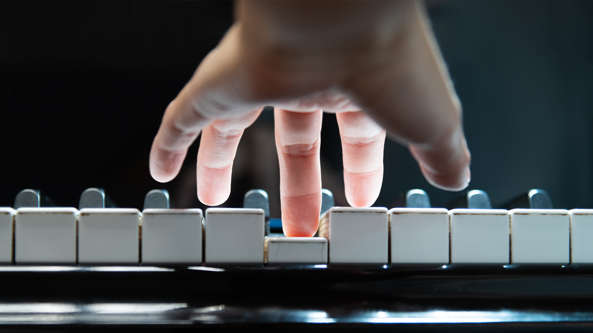 A hand over a piano keyboard, pressing a key with the middle finger