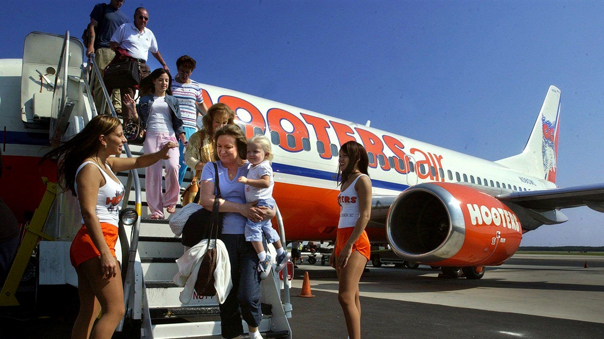 Hooters Air passengers exit the plane after a flight while being greeted by Hooters hostesses.