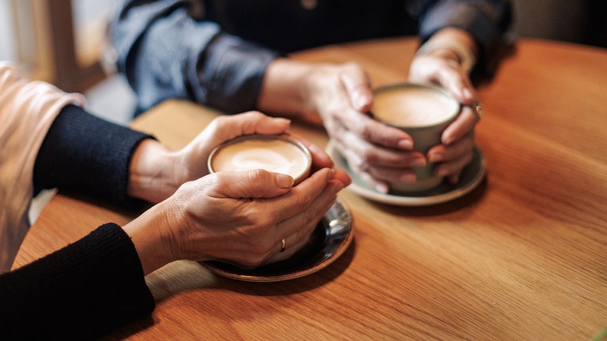 Adults holding coffees at table